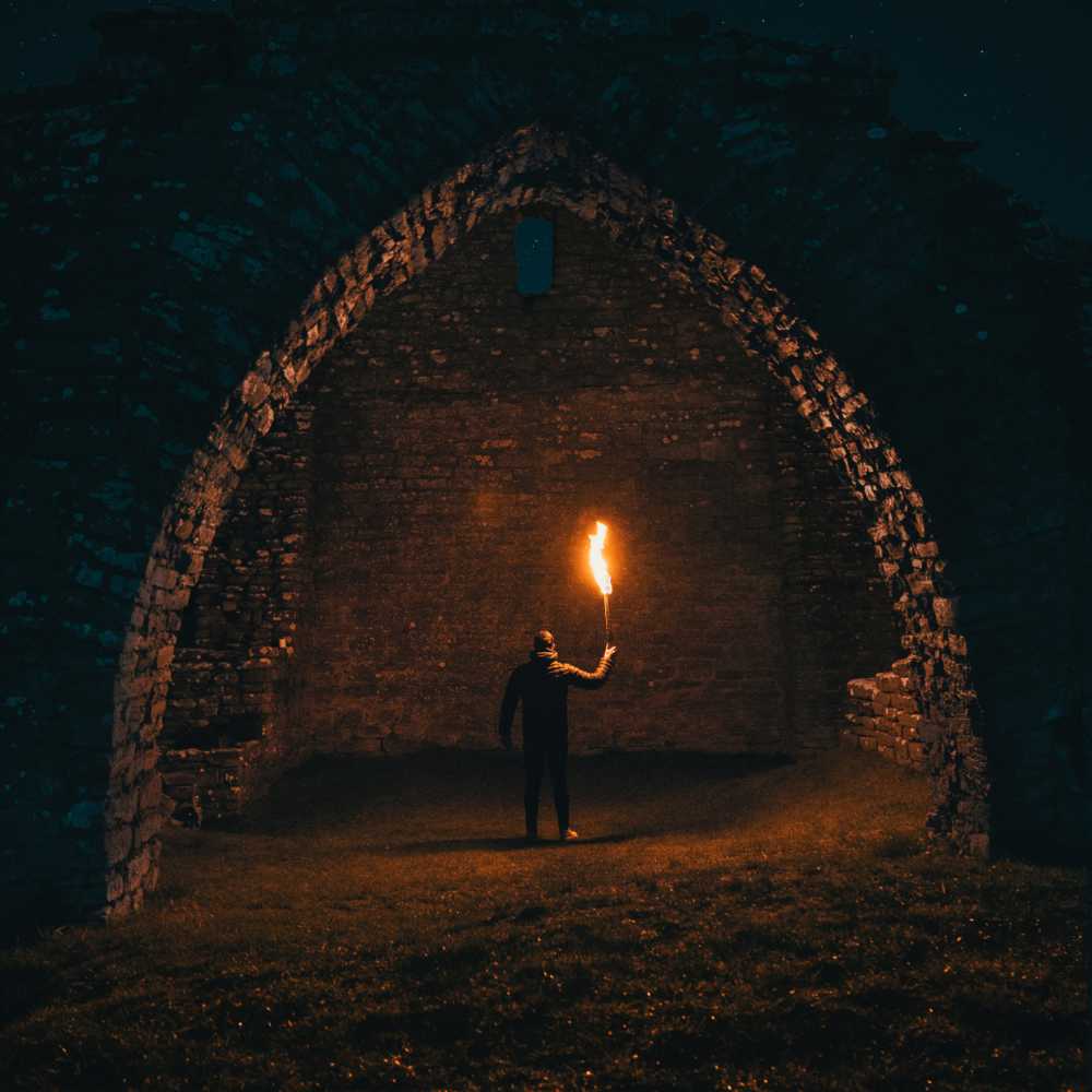 A man standing at a dark dungeon entrance with a torch